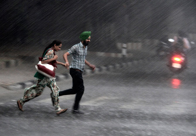 Commuters run for cover as they cross a road during monsoon rains in Chandigarh.