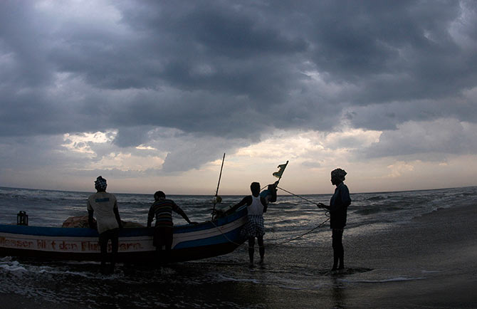 Indian fishermen stand with their boat against the backdrop of monsoon clouds on the marina beach in Chennai.