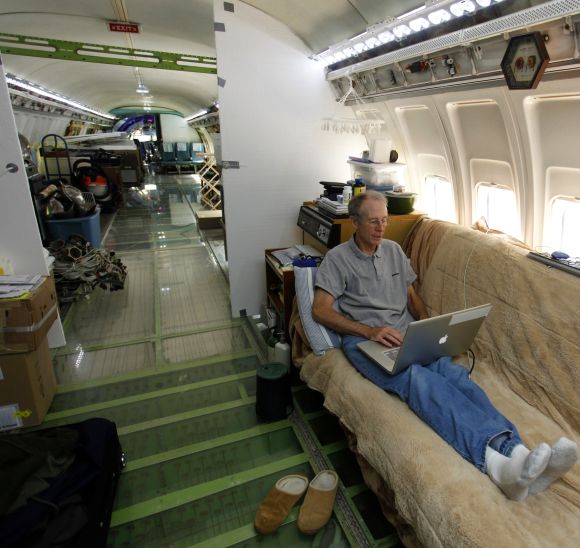 Bruce Campbell sits on his futon bed while using a laptop in his Boeing 727 home in the woods outside the suburbs of Portland.
