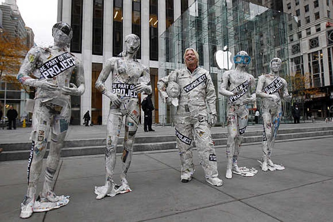 Richard Branson, dressed in a newspaper suit, stands next to mannequins outside New York City's flagship Apple store.