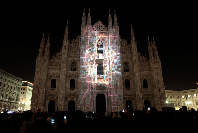 People take pictures during a video exhibition on the Duomo cathedral facade downtown in Milan, Italy