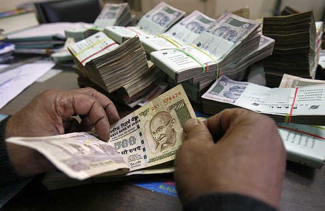 An employee counts Indian rupee notes at a cash counter inside a bank