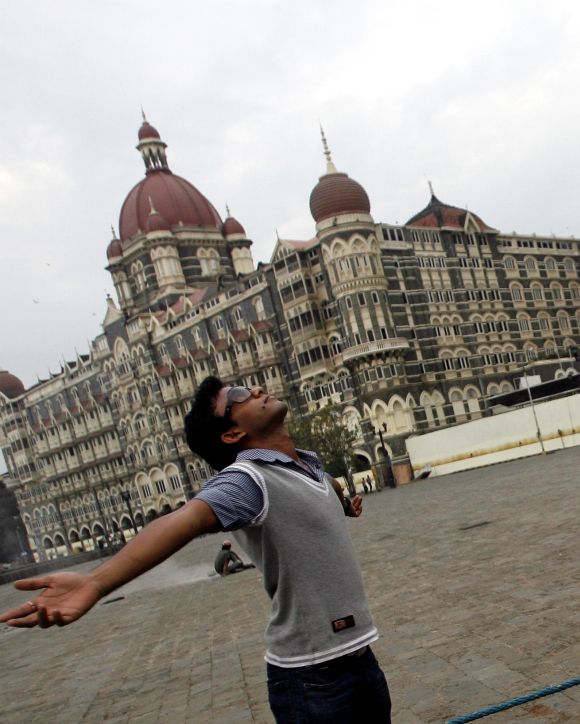 A visitor poses for a picture in front of Taj Mahal hotel in Mumbai.