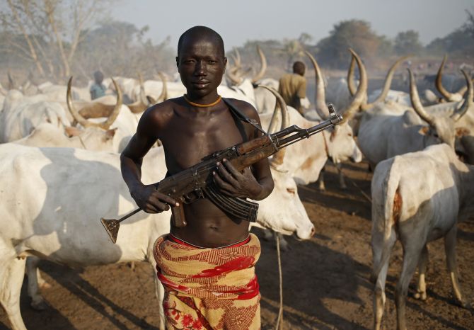 A man from Dinka tribe holds his AK 47 rifle in front of cow.