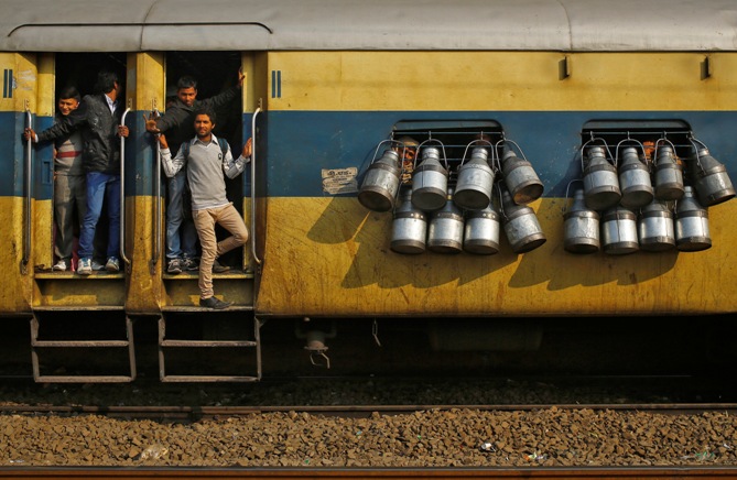 Commuters stand on the door of a passenger train as milk containers hang on the windows in Ghaziabad.