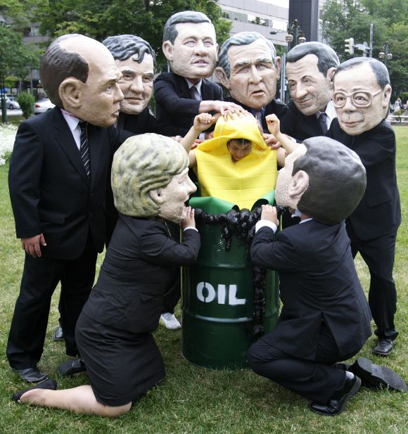 Activists from Oxfam, wearing masks depicting G8 leaders, place an activist dressed as a corn cob into an oil barrel in Sapporu.