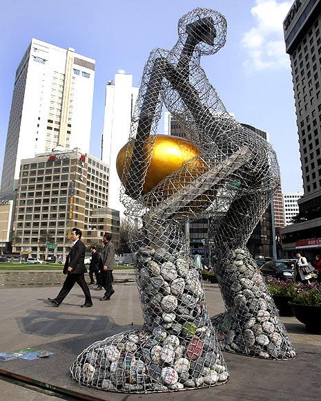 People walk past a statue titled 'Seoul broods a golden egg' at the Seoul city hall plaza in central Seoul.