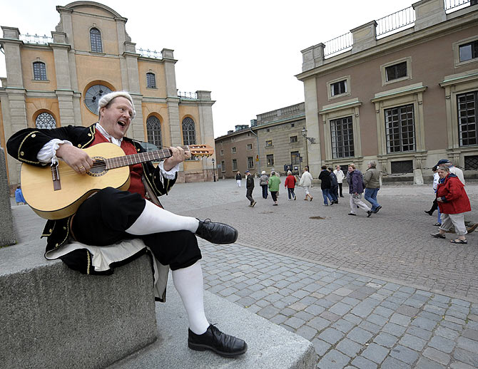 Tour guide Henrik Miko, dressed like the Swedish 18th century poet and composer Carl Michael Bellman, sings and plays his guitar in front of the Stockholm cathedral.