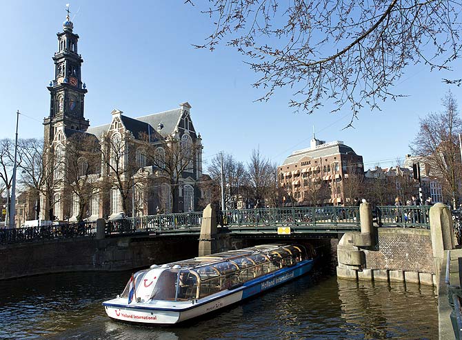 A tourist boat passes under a bridge next to the Westerkerk church in Amsterdam.