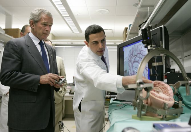 U.S. President George W. Bush (L) uses a remote control to deliver a simulated pacemaker to a part of a mockup human brain, as Ali Rezai, director of the center for advanced study of therapies for brain injury guides him, at the Cleveland Clinic in Ohio.