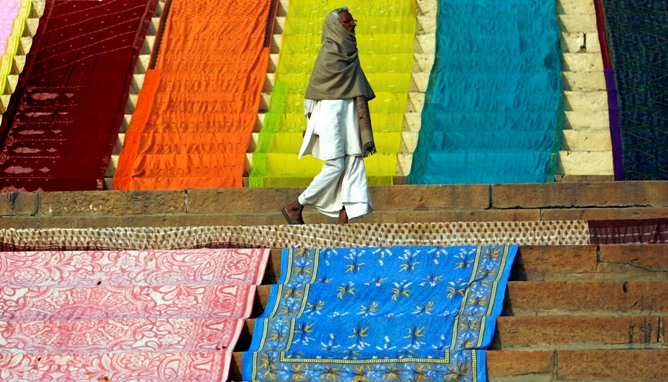 A man walks past Saris placed on the ground for drying by washermen on the banks of river Ganges in Varanasi.