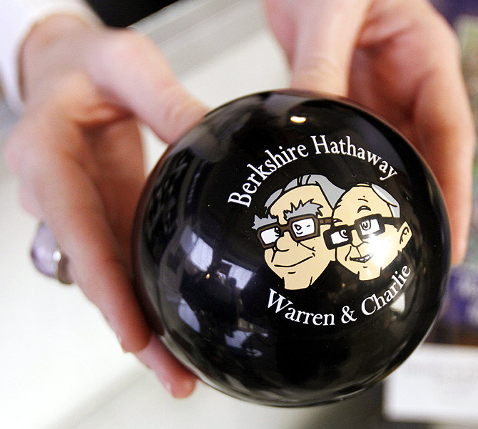 A clerk holds a magic answer ball featuring images of Berkshire Hathaway Chairman Warren Buffett (L) and Vice-Chairman Charlie Munger.