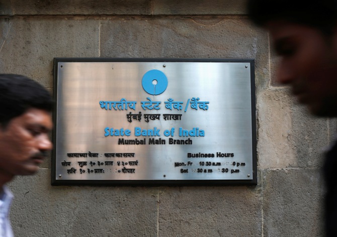 People walk in front of a signboard displayed at the head office of State Bank of India in Mumbai.