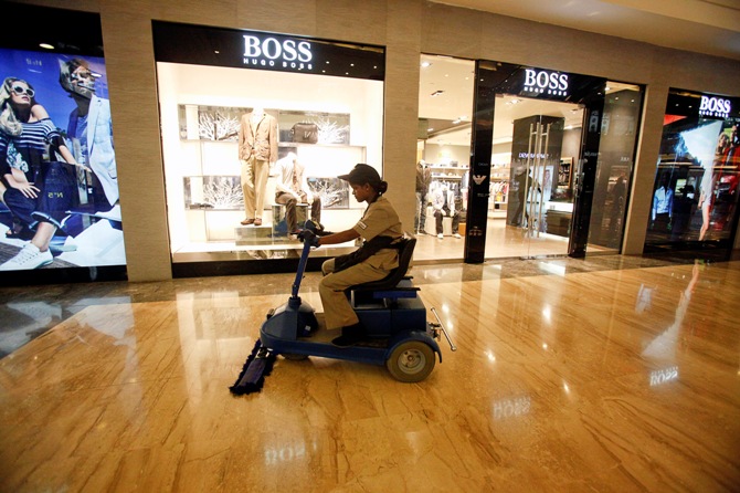 An employee operates a floor cleaning machine in front of a Hugo Boss showroom inside a shopping mall.