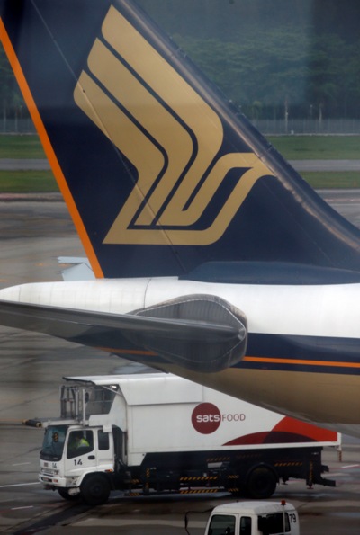 An in-flight catering truck passes a Singapore Airlines plane sitting on the tarmac.