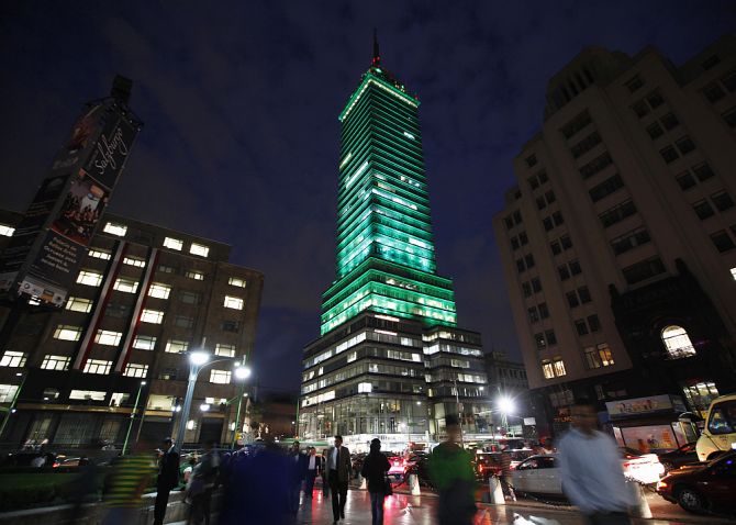 Pedestrians walk past the Torre Latinoamericana illuminated by LED lights, part of an artistic intervention, in downtown Mexico City.