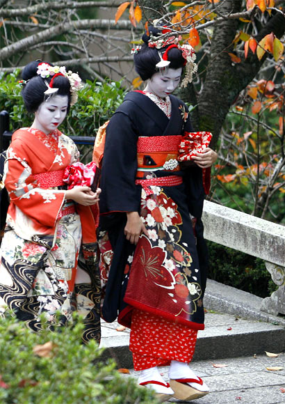 Women in traditional makeup and kimonos walk inside the Kiyomizudera temple during autumn in Kyoto.