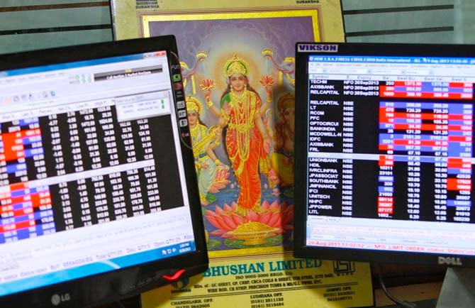 An image of Goddess Lakshmi is placed between monitors displaying share price index at a share trading market.