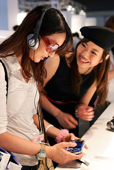 A woman plays Sony's PlayStation Portable (PSP) while a booth assistant (R) advises her during Tokyo Game Show.