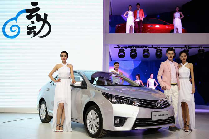 Models stand beside the Toyota Corolla cars during the 2014 Beijing International Automotive Exhibition.