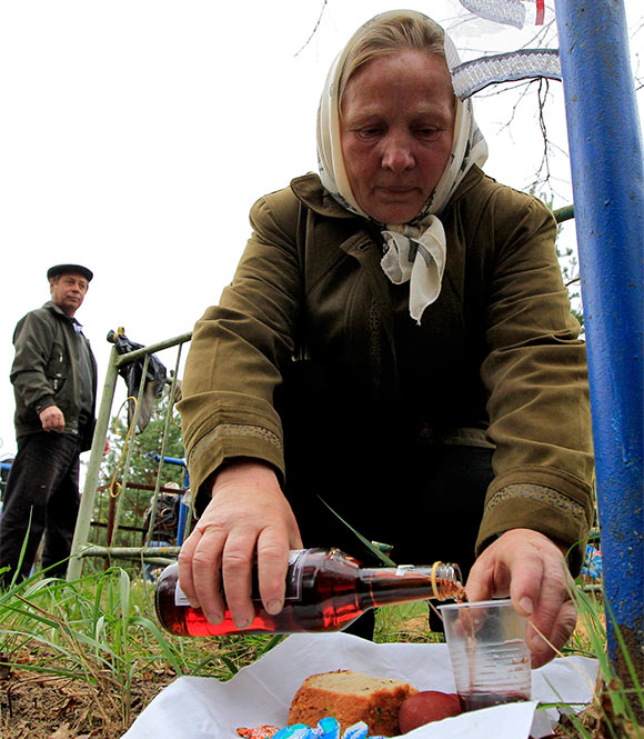 A woman fills a glass with wine at a grave in a cemetery during Radunitsa, or the Day of Rejoicing.