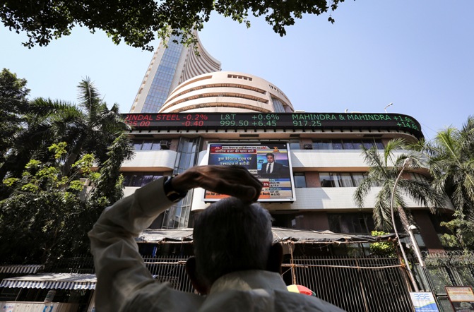 A man looks at a screen across the road displaying the Sensex on the facade of the Bombay Stock Exchange.