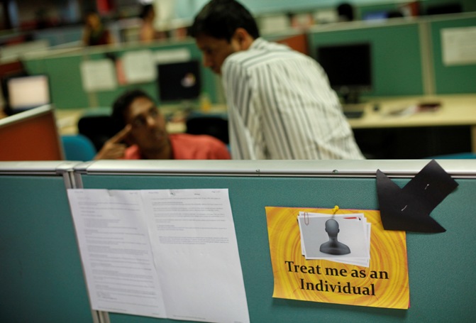 Employees work behind a sign that reads 'treat me as an individual' on the floor of the outsourcing company in Mumbai. 