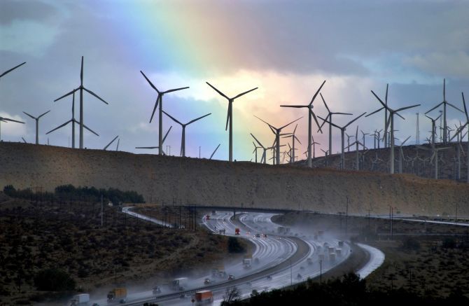 A rainbow forms behind giant windmills.