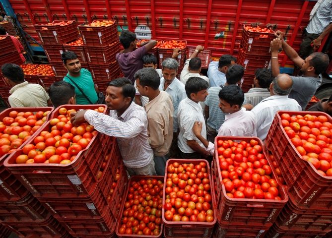 Customers crowd amid stacked baskets of tomatoes at a wholesale vegetable and fruit market in Chandigarh.