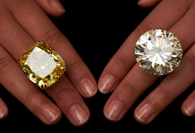 A model poses with a vivid yellow 100.09 carats diamond (L) and a 103.46 carats diamond ring during an auction preview at Sotheby's in Geneva.
