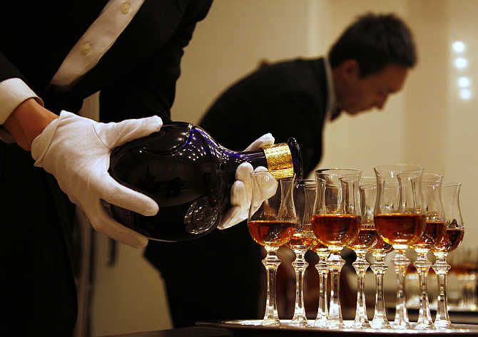 A waiter is reflected in a mirror as he pours whisky in Beijing, China.