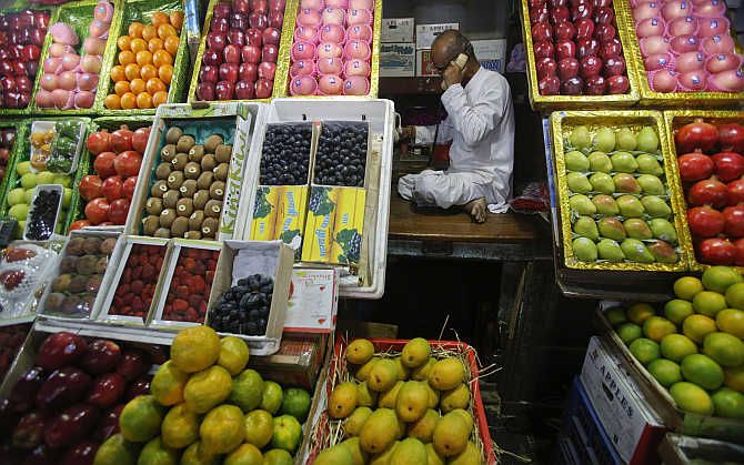 A fruit vendor speaks on his phone while sitting at his fruit stall at a wholesale market in Mumbai.