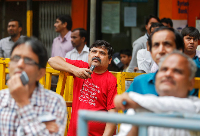 Worried traders look at the Sensex figures displayed on a screen at the Bombay Stock Exchange