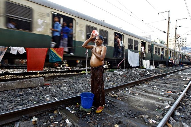 A man takes a bath on a railway track next to a train passing through a slum area