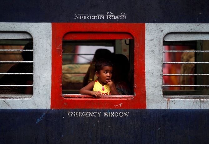A girl looks out through an open emergency window of a passenger train at a railway station. 