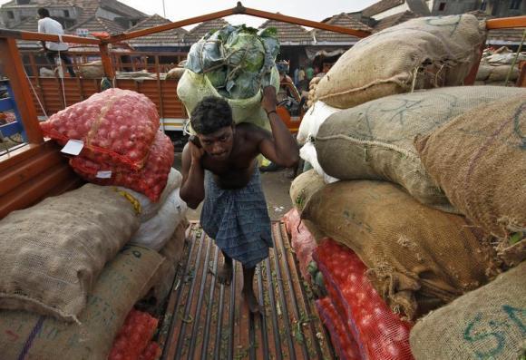 A labourer carries a sack filled with cabbage to load it onto a supply van at a vegetable wholesale market in Chennai.