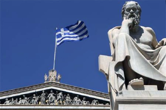 A Greek flag flutters behind a statue of ancient philosopher Socrates at the the Academy of Athens. 