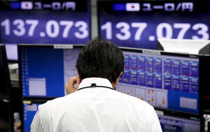 An employee of a foreign exchange trading company stands in front of monitors displaying the current exchange rate of the Japanese yen against the Euro in   Tokyo June 30, 2015.