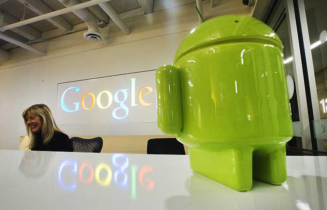 A Google Android figurine sits on the welcome desk as employee Tracy McNeilly smiles at the Google office in Toronto, Canada.