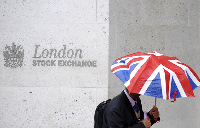 A worker shelters from the rain as he passes the London Stock Exchange in the City of London 