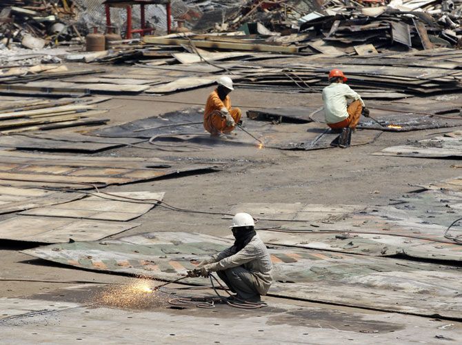 Workers dismantle steel plates of a decommissioned ship at the Alang shipyard