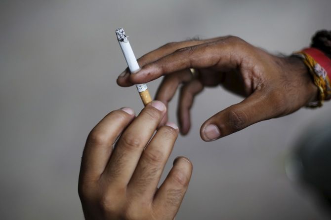 Image: A man passes a cigarette to another while smoking as they sit on a pavement along a road in New Delhi. Photograph: Adnan Abidi/Reuters 