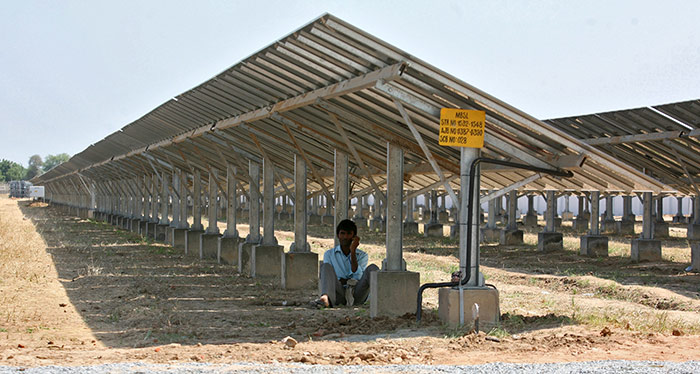A worker speaks on a mobile phone as he sits under the installed solar panels of a newly inaugurated solar farm at Gunthawada village in Banaskantha district, Gujarat. Photo: Amit Dave/Reuters