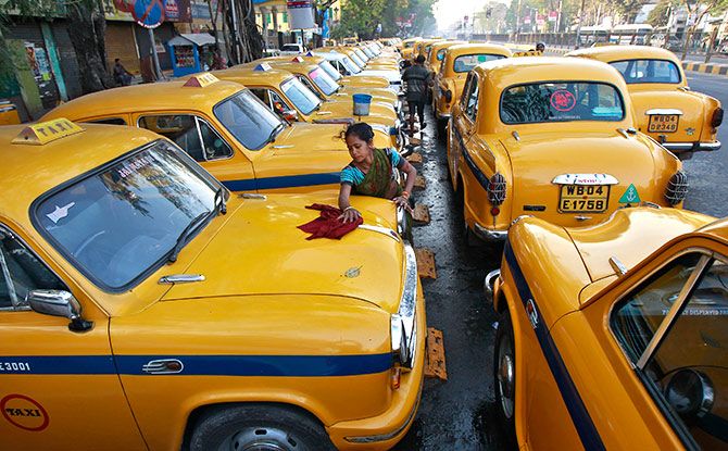 Sumitra Sarkar, 35, cleans a yellow ambassador taxi at a parking area along a roadside in Kolkata. Photograph: Rupak De Chowdhuri/Reuters.