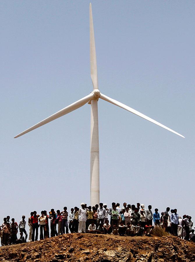 Villagers stand under a power generating windmill turbine during the inauguration ceremony of the new 25 MW ReNew Power wind farm at Kalasar village in the western Indian state of Gujarat. Photograph: Amit Dave/Reuters 