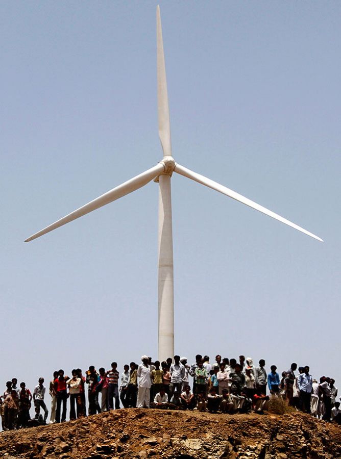 Villagers stand under a power generating windmill turbine during the inauguration ceremony of the new 25 MW ReNew Power wind farm at Kalasar village in the western Indian state of Gujarat. Photograph: Amit Dave/Reuters 