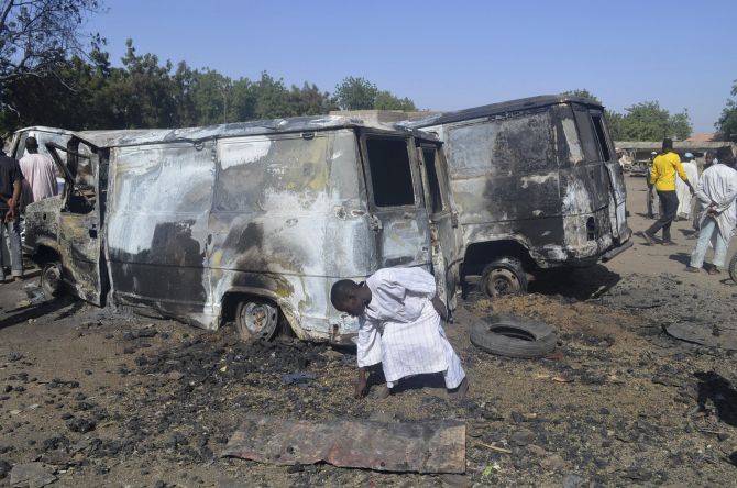 A boy searches the ground next to a burnt-out vehicle, caused by an attack from Boko Haram militants, in Bama, Borno 