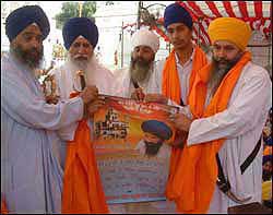 Bhai Manjit Singh, Amrik Singh's brother, and others holding a calendar depicting a shattered Akal Takht