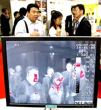 Visitors walk behind a NEC Avio Infrared Technologies Co's thermo graphic examination system for use in detecting the H1N1 virus at the Office Security Expo in Tokyo
