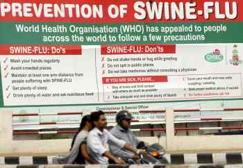 People ride past a billboard carrying messages on swine flu prevention in Hyderabad